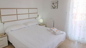 Un lit bien fait, avec des draps blancs, une lampe de chevet et une serviette pliée posée sur la table de chevet.