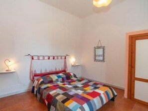 A bedroom with a colorful quilted bedspread, a bedside lamp, a wall-mounted mirror, and a wooden door. - Camilla by Interhome (Valledoria)