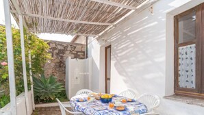 A patio with a table set for breakfast, surrounded by white chairs, under a thatched roof. - Camilla by Interhome (Valledoria)