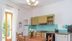 A compact kitchen with a dining area, featuring a round wooden table and chairs, a small refrigerator, and a tiled backsplash. - Camilla by Interhome (Valledoria)