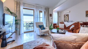 Una sala de estar moderna con televisor de pantalla plana, asientos cómodos, comedor y balcón con mobiliario exterior.