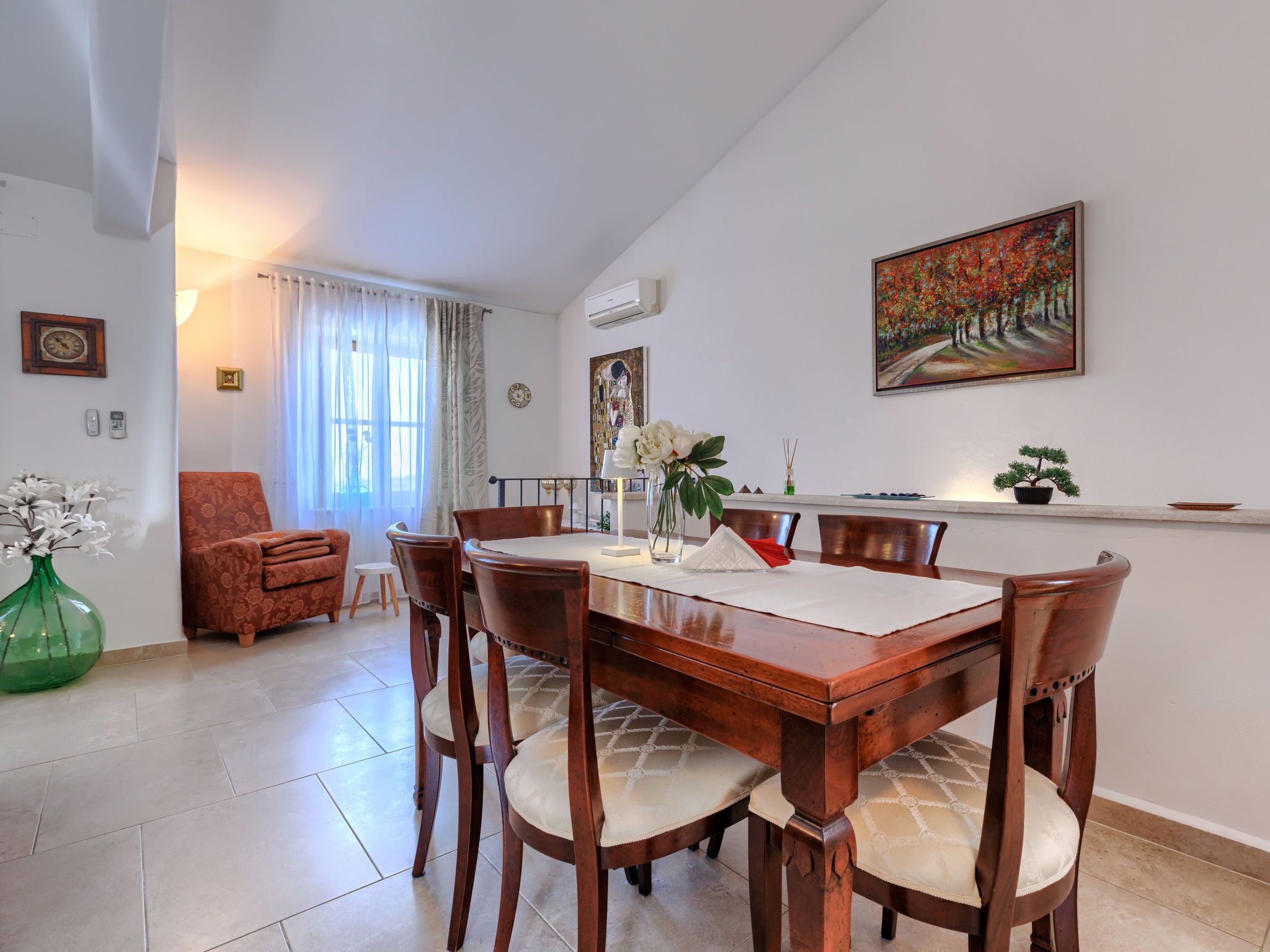A dining area with a wooden table and chairs, a vase with flowers, and a painting on the wall.