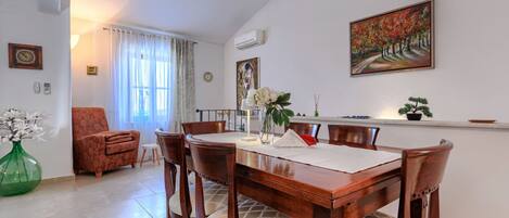 A dining area with a wooden table and chairs, a vase with flowers, and a painting on the wall.