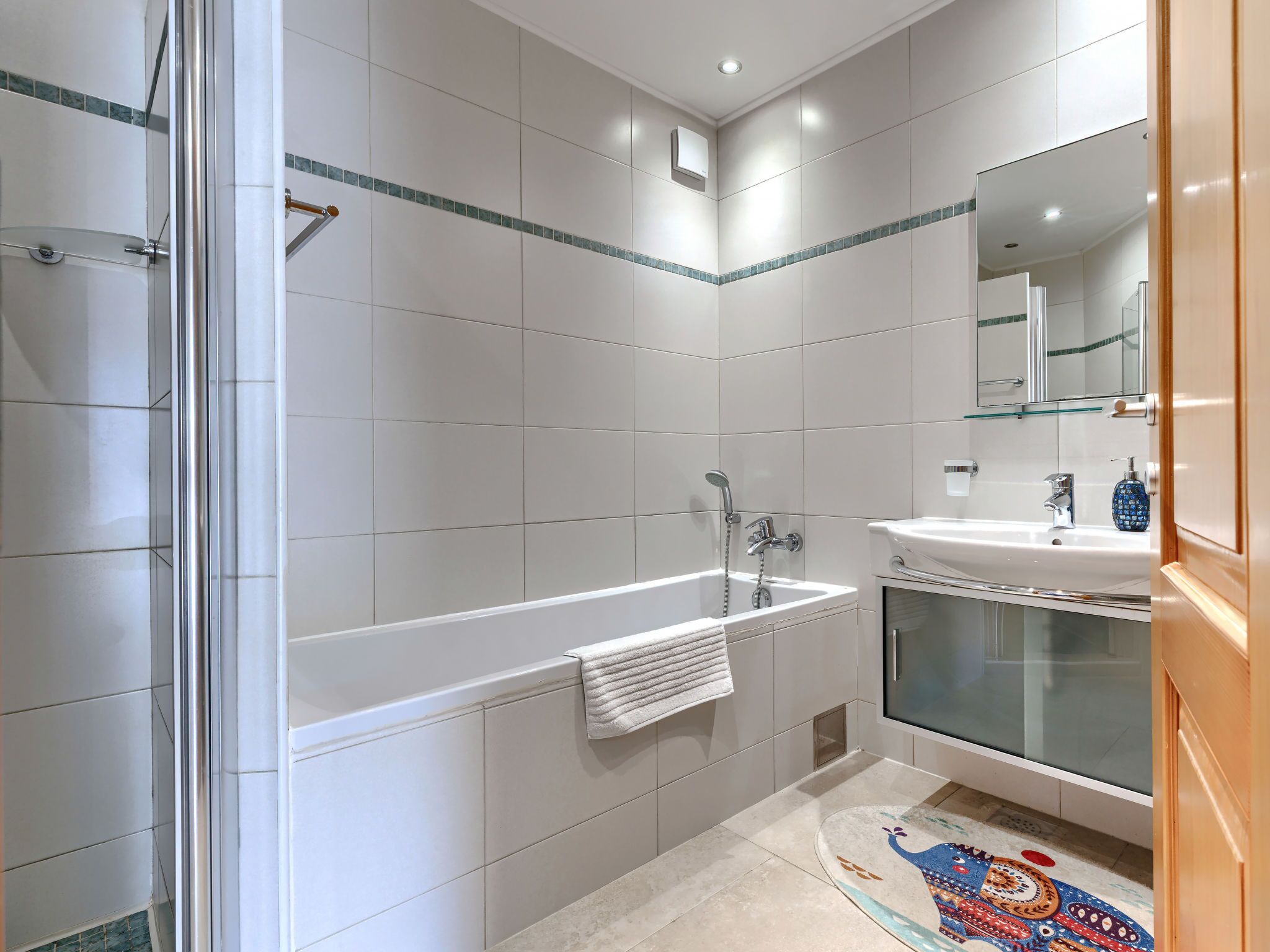 A modern bathroom with a glass-enclosed shower, a freestanding bathtub, a sink with a mirror, and a decorative rug.