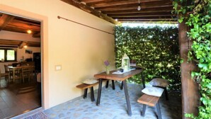 An outdoor patio with a wooden table and benches, surrounded by greenery and a stone floor. - Casa la Selvolina by Interhome (Roccastrada)