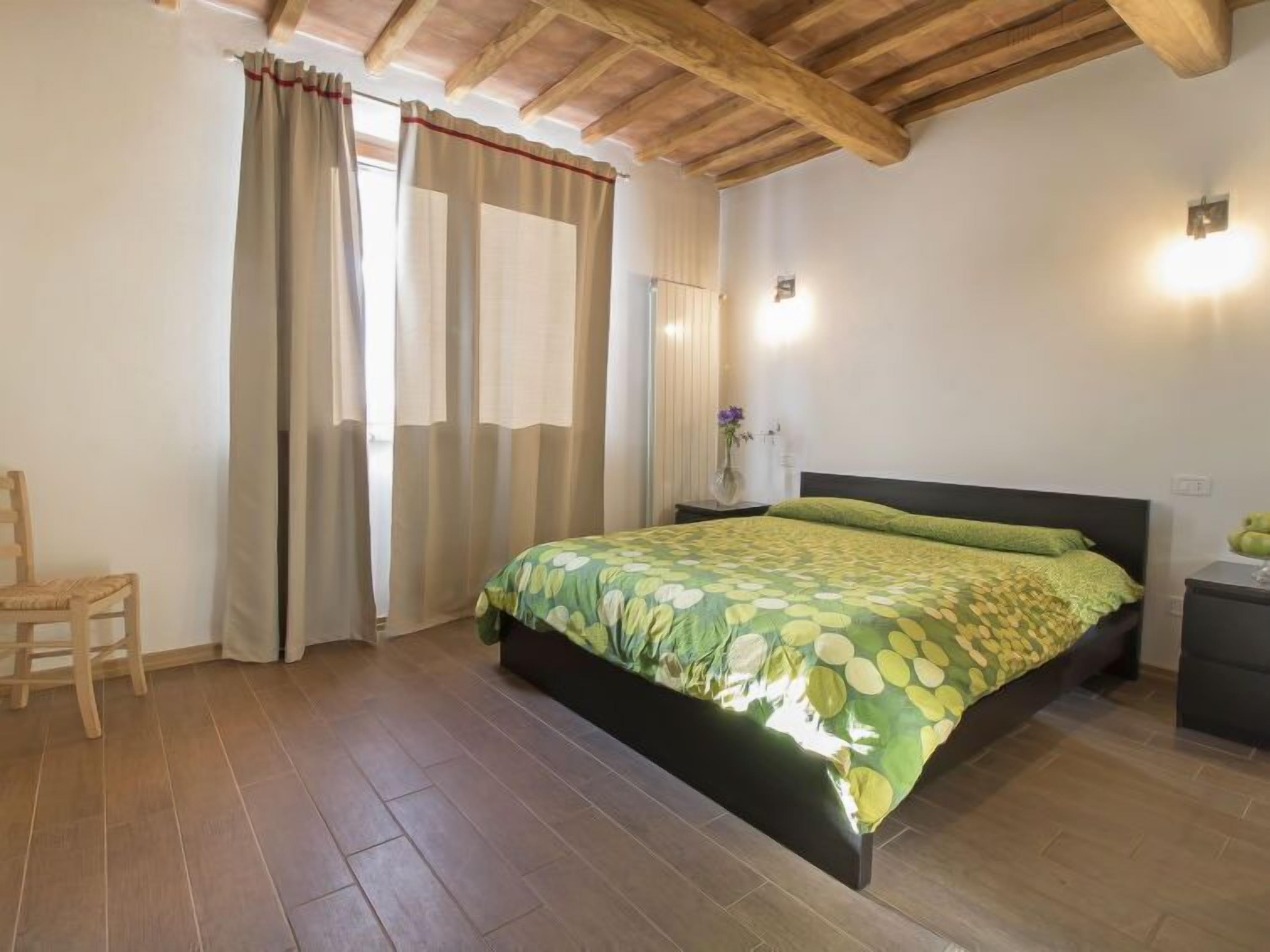 Un dormitorio con cama, piso de madera, cortinas y una silla.