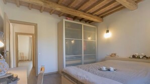 A bedroom with a large bed, a wooden ceiling, a sliding glass door, and a bedside table with a cup and saucer. - Casa la Selvolina by Interhome (Roccastrada)
