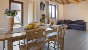 A dining area with a wooden table, chairs, and a fruit bowl. There is a sofa and a TV in the background. - Casa la Selvolina by Interhome (Roccastrada)