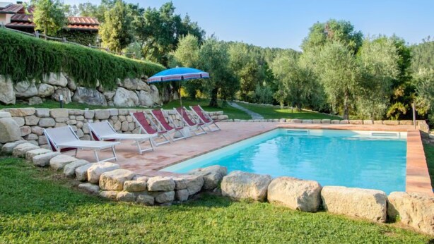 A swimming pool with lounge chairs and a stone wall. - Casa la Selvolina by Interhome (Roccastrada)