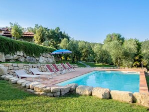 Una piscina con sillas de descanso y un muro de piedra.