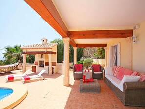 A covered outdoor area with a pool, lounge chairs, a sofa, and a small table.