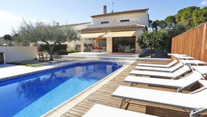 A swimming pool with lounge chairs, a wooden deck, and a modern house in the background. - Perales by Interhome (L'Ampolla)