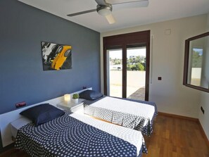 A bedroom with two beds, a ceiling fan, a window with a view of the outside, and a painting on the wall. - Perales by Interhome (L'Ampolla)