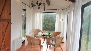 Une pièce chaleureuse avec une table à manger et deux chaises en osier, une porte en bois et une grande fenêtre avec des rideaux.