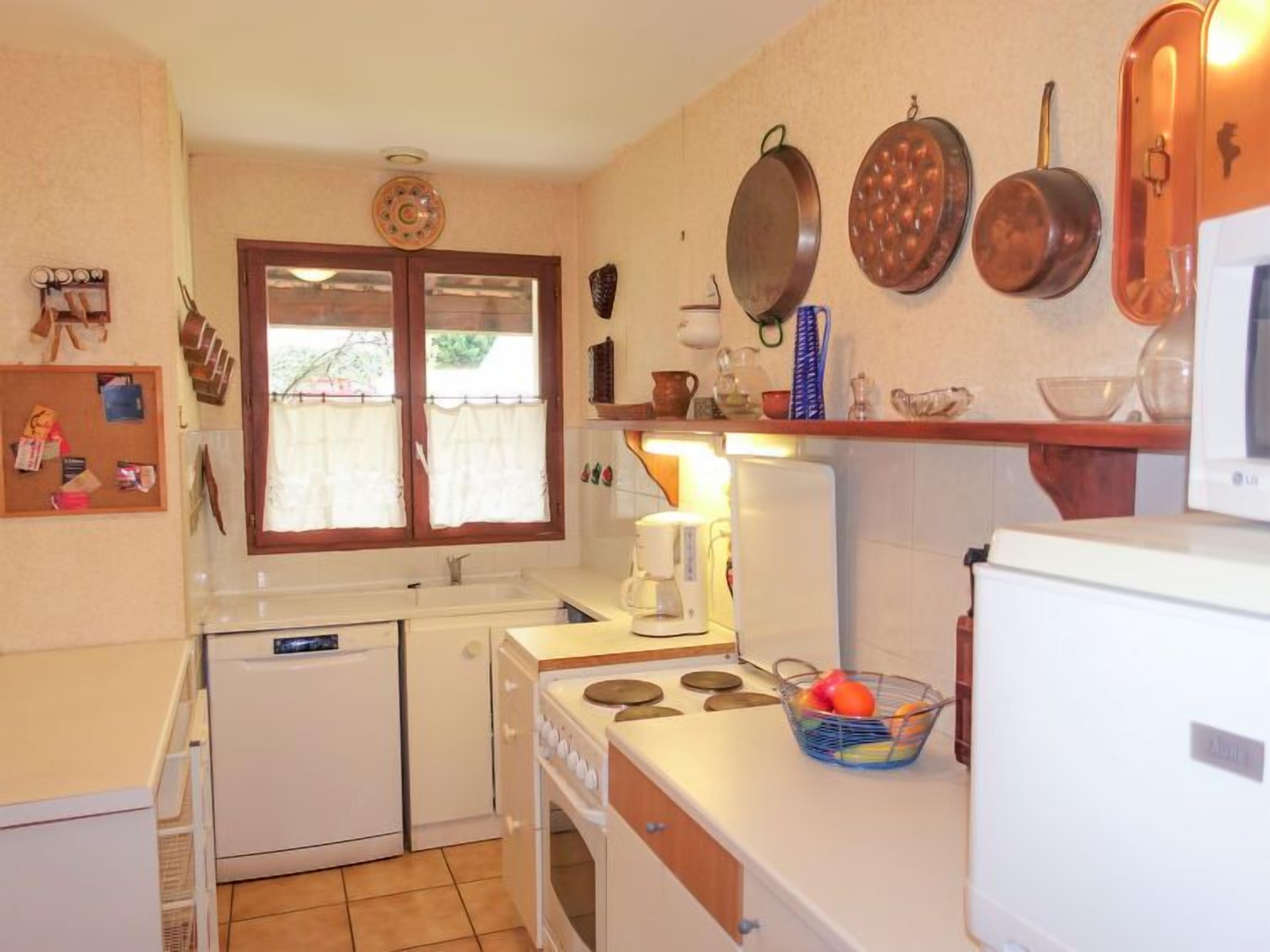 Une cuisine compacte équipée d’une cuisinière, d’un évier et d’un four à micro-ondes. On y trouve une fenêtre avec des rideaux, un réfrigérateur et un petit égouttoir.