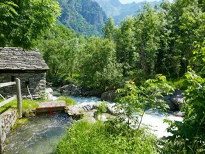 Ein aus Stein errichtetes Gebäude mit Holzzaun, einer kleinen Brücke und einem Fluss in einem üppigen, grünen Tal.