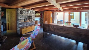 A rustic interior with exposed wooden beams, a stone fireplace, a wooden bench, and a view of the outside.