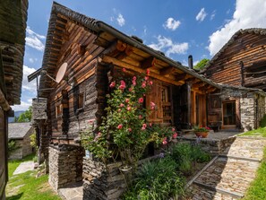 A rustic wooden house with a stone foundation, a wooden porch, and a garden with flowering plants.
