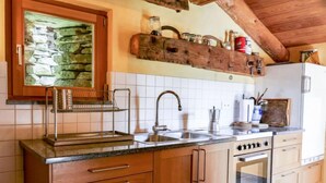 A kitchen with wooden cabinets, a stone backsplash, a built-in oven, and a hanging rack above the sink.