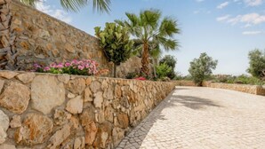 A stone wall with a tiled pathway, surrounded by greenery and palm trees. - Villa Pescada by Interhome (Albufeira)