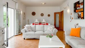 A spacious living room with a white sofa, a coffee table, and a dining area with a red tablecloth. - Villa Pescada by Interhome (Albufeira)
