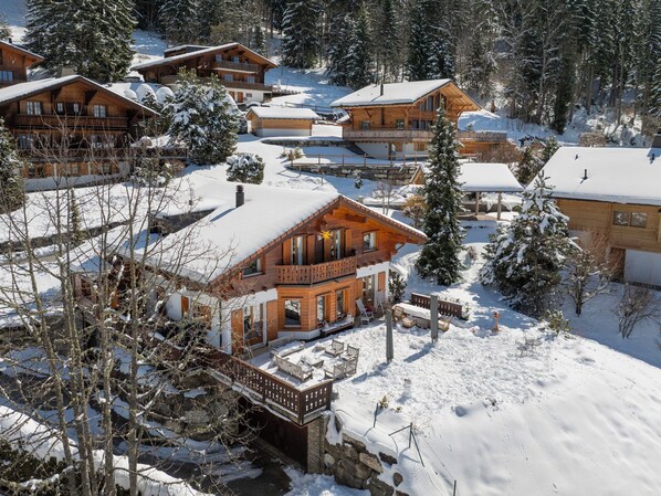 A snow-covered lodge with multiple wooden buildings, a stone bridge, and snow-covered trees.