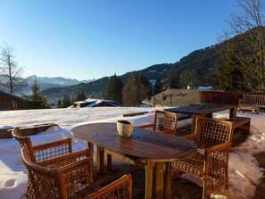 Relax in a serene outdoor seating area with a round table and wicker chairs, surrounded by breathtaking mountain views.
