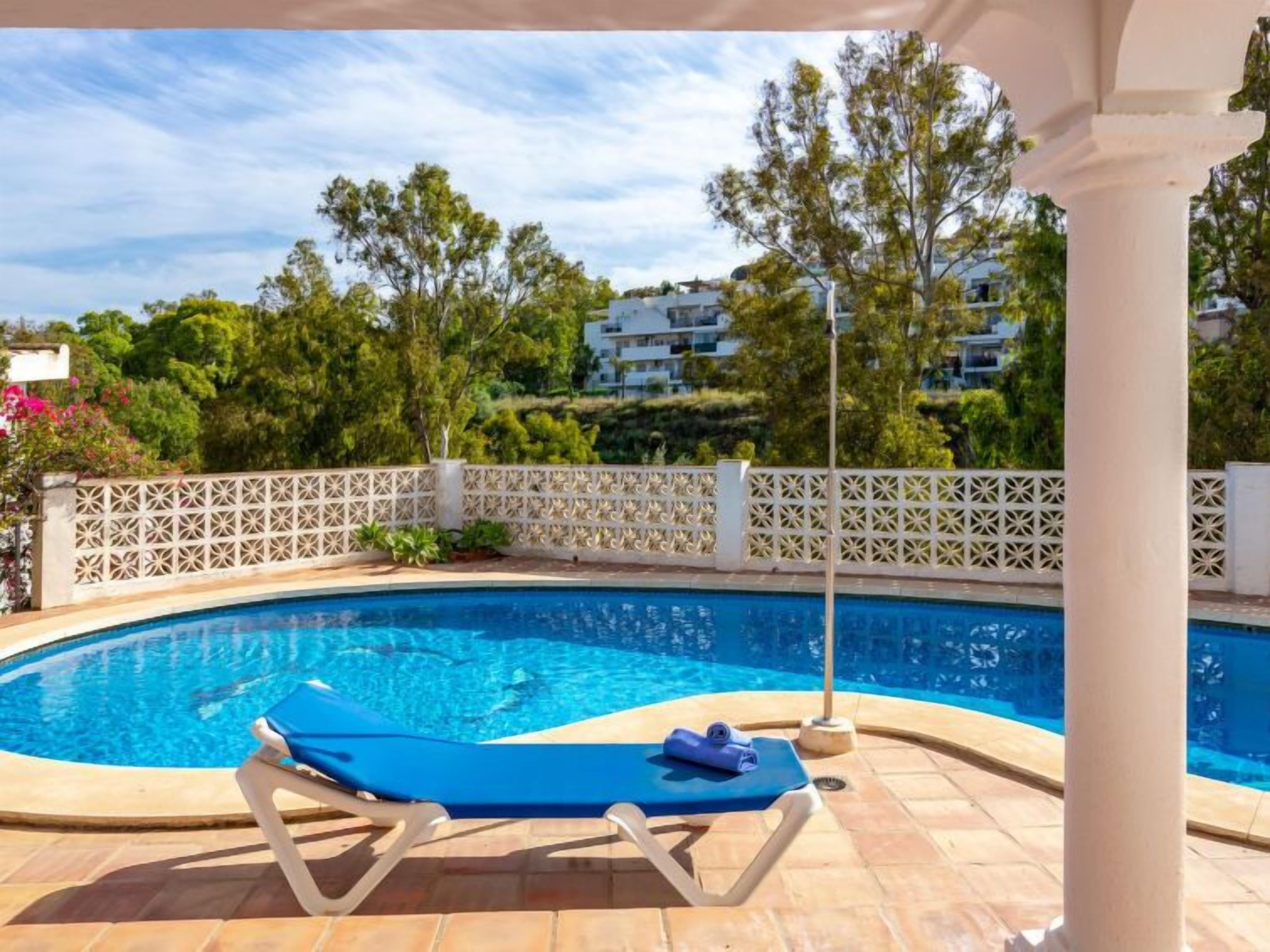 Ein Swimmingpool mit weißem Gitterzaun, einem blauen Liegestuhl und einer Pergola.
