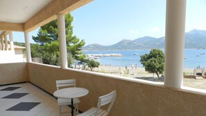 Een balkon met een tafel en stoelen, met uitzicht op een strand met boten en bergen in de verte.