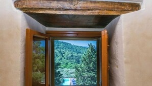 Une pièce dotée d’une porte en bois qui donne sur un balcon offrant une vue sur une colline boisée.