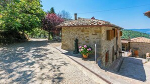 Un bâtiment en pierre avec un toit en tuiles, une allée gravillonnée et un pot de fleurs contenant une plante aux fleurs roses.
