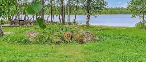 Une propriété située au bord d’un lac, dotée d’une pelouse, d’une terrasse en bois avec des chaises et offrant une vue sur l’eau.