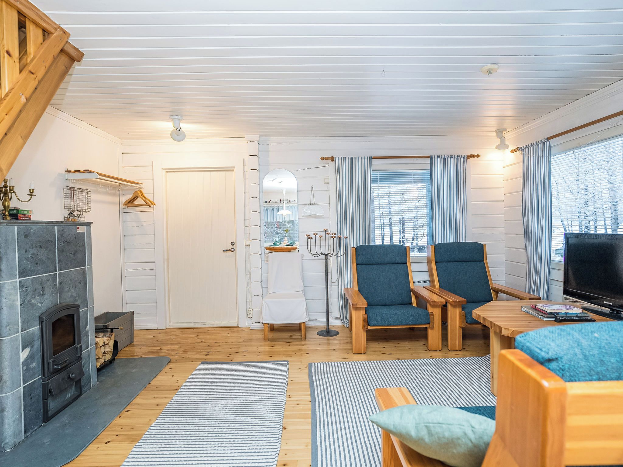 Ein gemütliches Wohnzimmer mit Kamin, zwei blauen Sesseln, einem Holztisch und einem Fernseher.