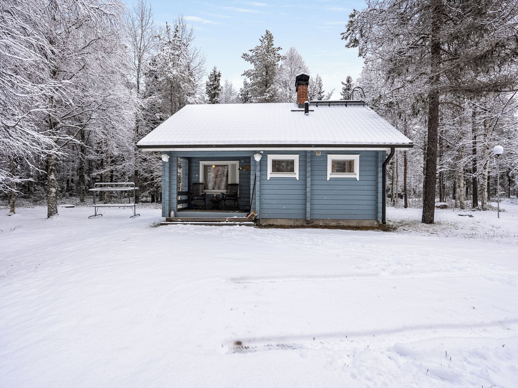 Una cabana petita d'un pis amb un teulat cobert de neu, envoltada d'arbres en un paisatge nevós.