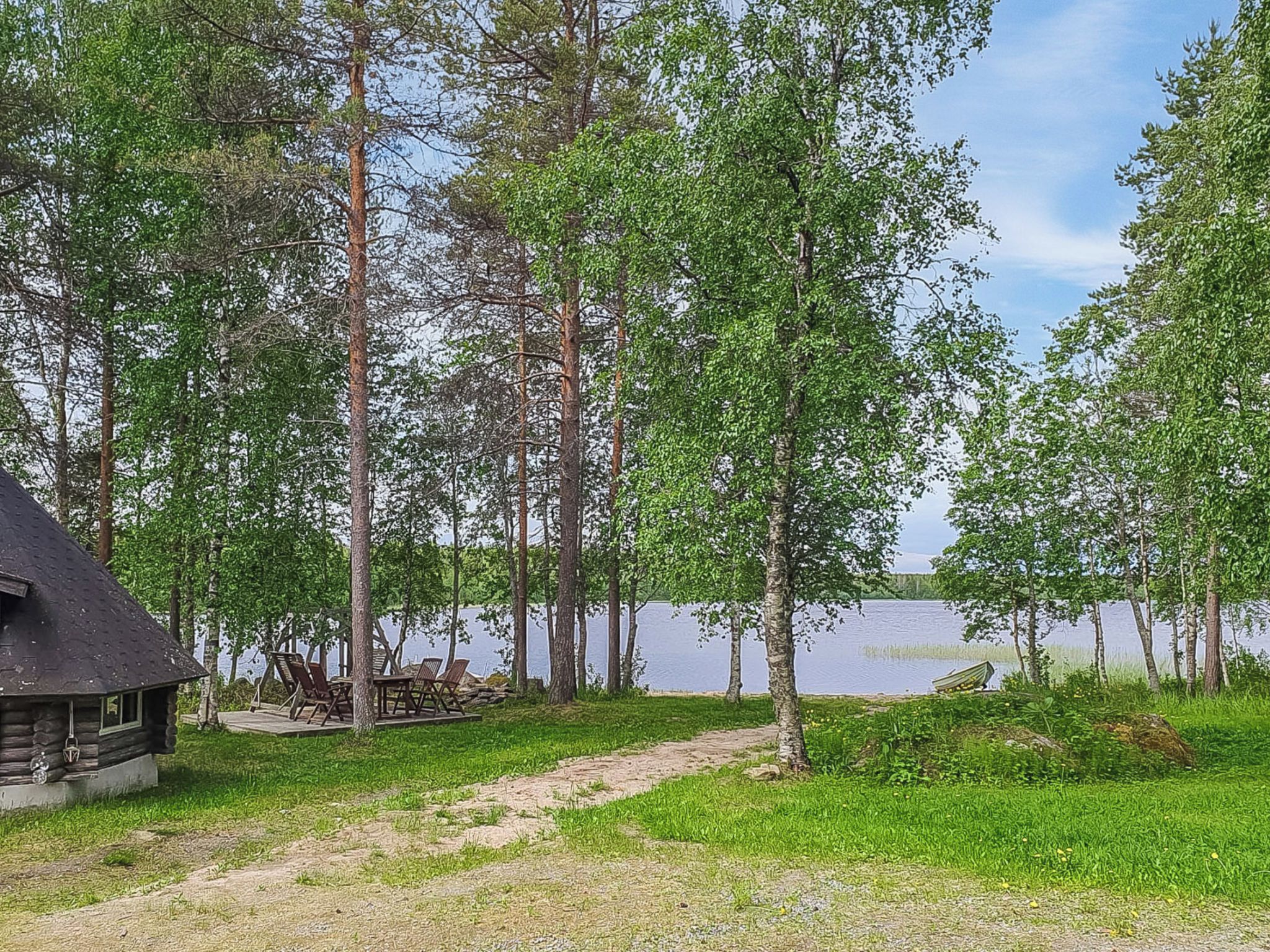 Une cabane dotée d’une terrasse et de meubles de jardin, entourée d’arbres et bordée par un lac.