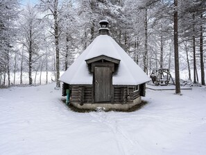 A snow-covered wooden cabin with a steep roof and a central chimney, surrounded by a forest. - Keloranta by Interhome (Kuusamo)