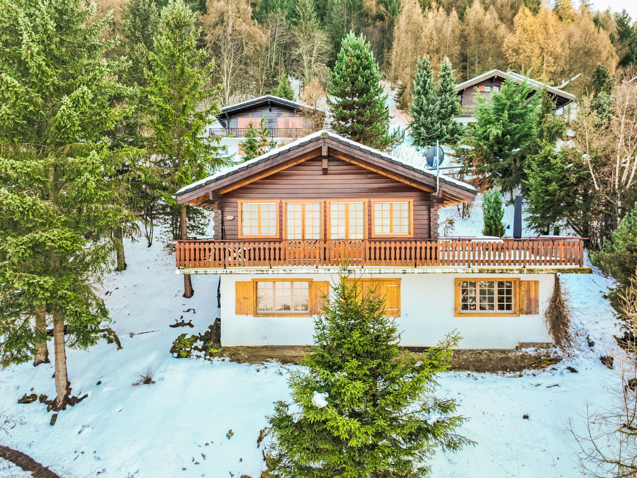 Una cabaña de madera con balcón, rodeada de nieve y árboles.