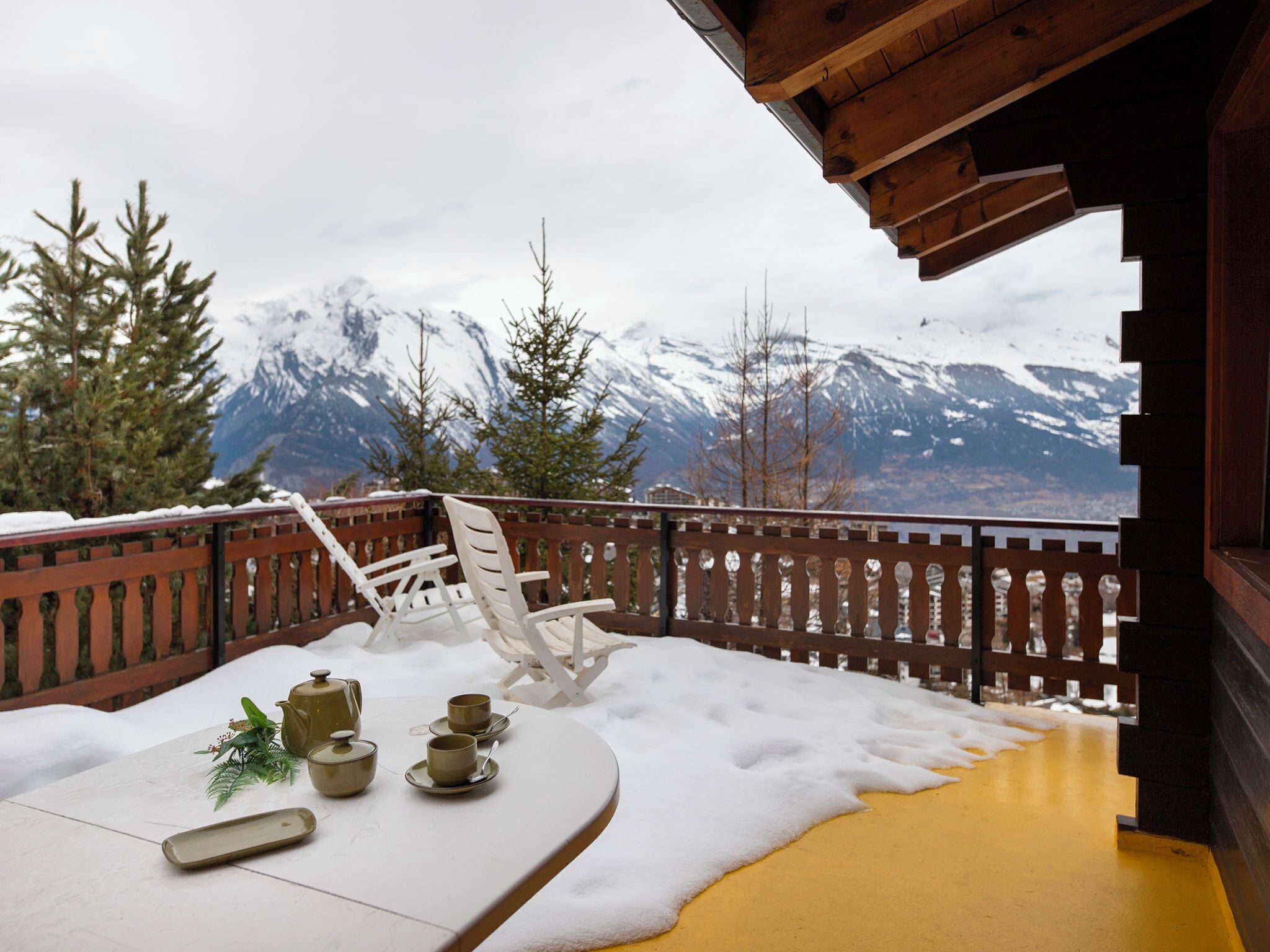 Eine Holterrasse mit einem für Tee gedeckten Tisch, mit Blick auf schneebedeckte Berge.
