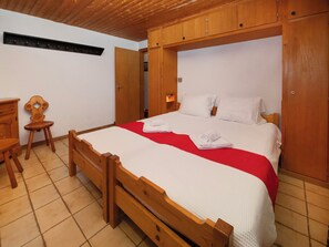 A wooden bed with a red blanket, a wooden nightstand, and a chair.