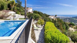 A pool with a stone border, a palm tree, and a view of a coastal town. - Lausanne by Interhome (Calonge)