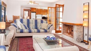 A living room with a sofa, a glass coffee table, a fireplace, and a ceiling fan. - Lausanne by Interhome (Calonge)