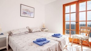 A bedroom with two beds, a large window, a chair, and a framed picture on the wall. - Lausanne by Interhome (Calonge)