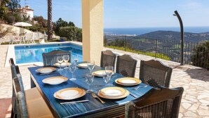 A dining area with a table set for four, overlooking a pool and a scenic view of hills and the sea. - Lausanne by Interhome (Calonge)