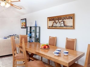 A dining area with a wooden table, chairs, and a fruit bowl. There is a bookshelf with books and decorative items, and a painting on the wall. - Lausanne by Interhome (Calonge)