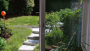 Eine Terrasse mit Holzdeck, einem gepflasterten Weg und Blick auf einen Garten.