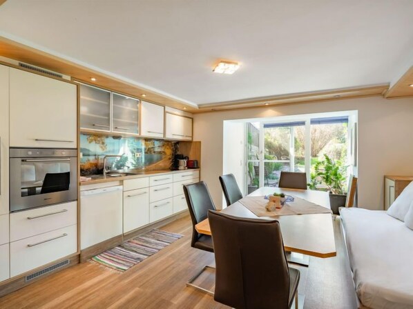 A modern kitchen with white cabinets, a built-in oven, and a dining area with a table and chairs.