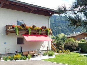 A building with a balcony adorned with flowers, a red awning, and a view of a mountainous landscape.