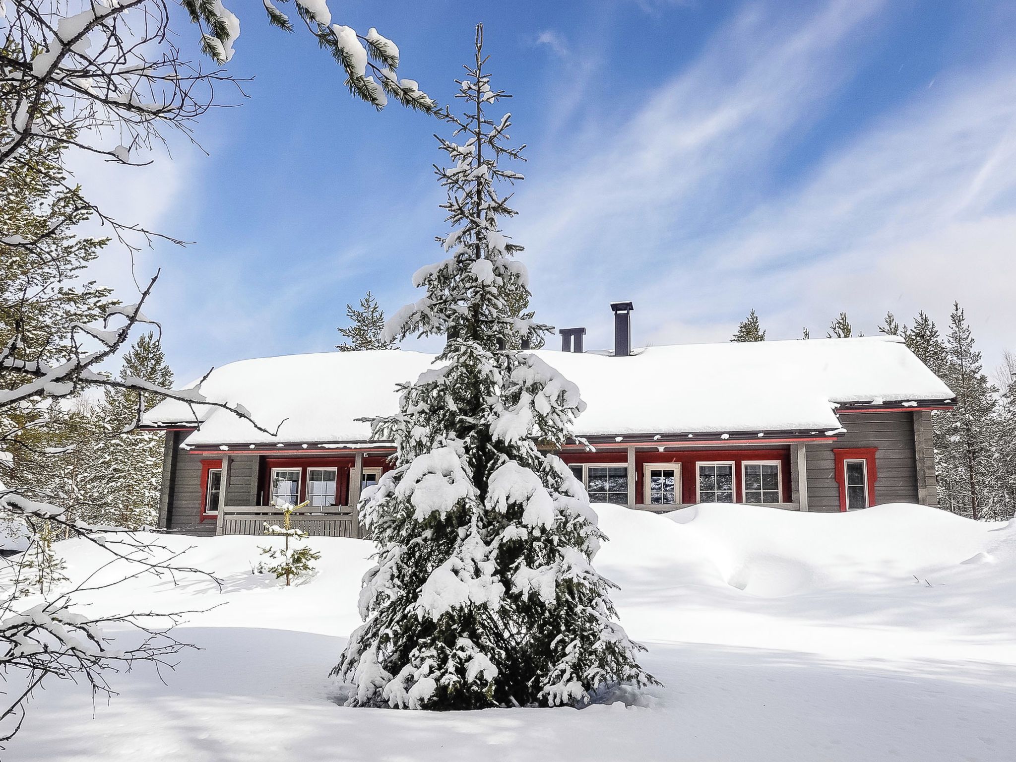 Paisatge nevat amb una casa que té façana vermella i teulada coberta de neu.