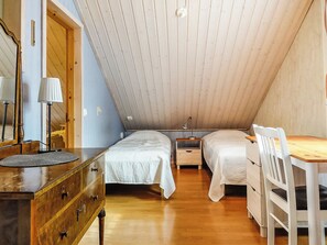 A room with a sloped ceiling, two beds, a wooden dresser, a table with chairs, and a lamp. - Lustola a by Interhome (Sodankylä)