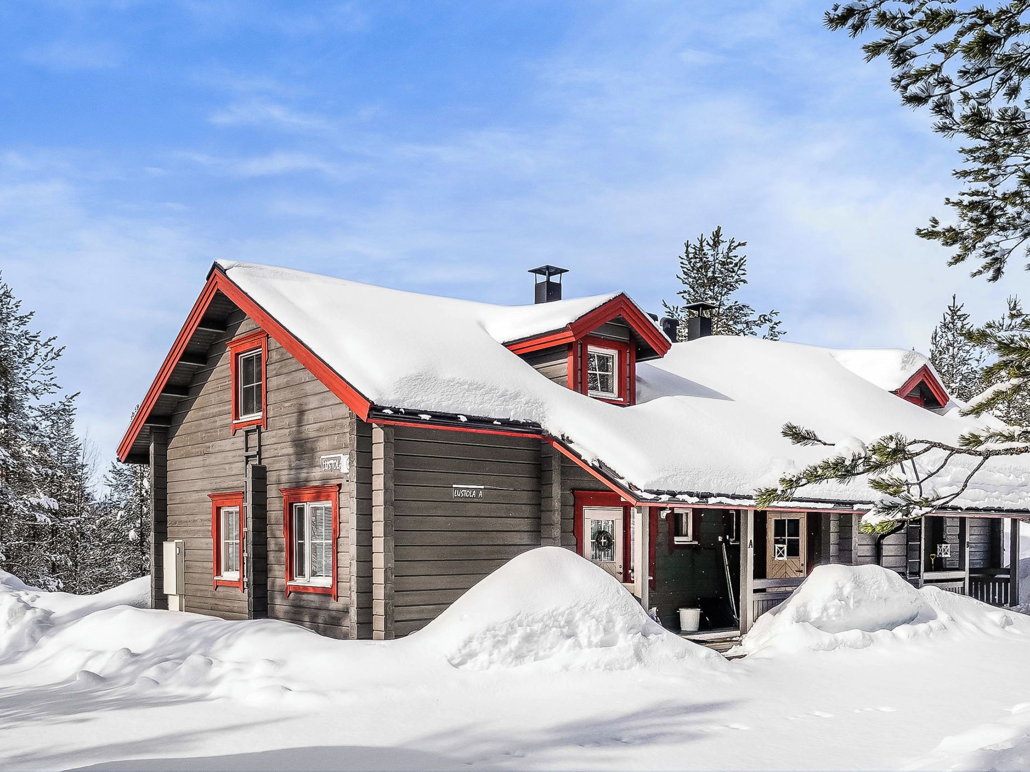 Una casa de madera de dos pisos con techo rojo y paisajes nevados.
